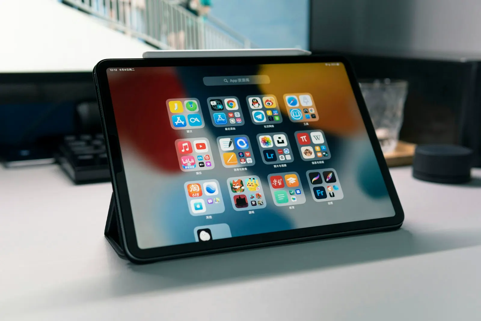 An iPad Pro in a stand on a desk showing its home screen