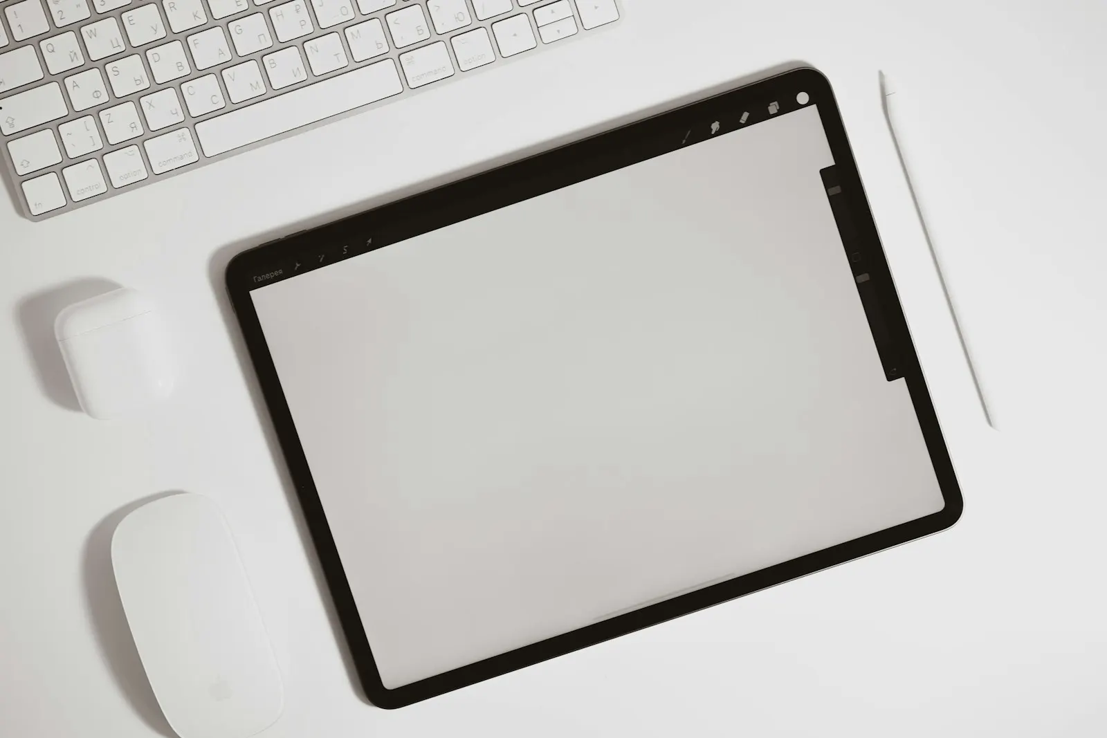 An iPad Pro with a blank screen lying on a white desk beside a keyboard
