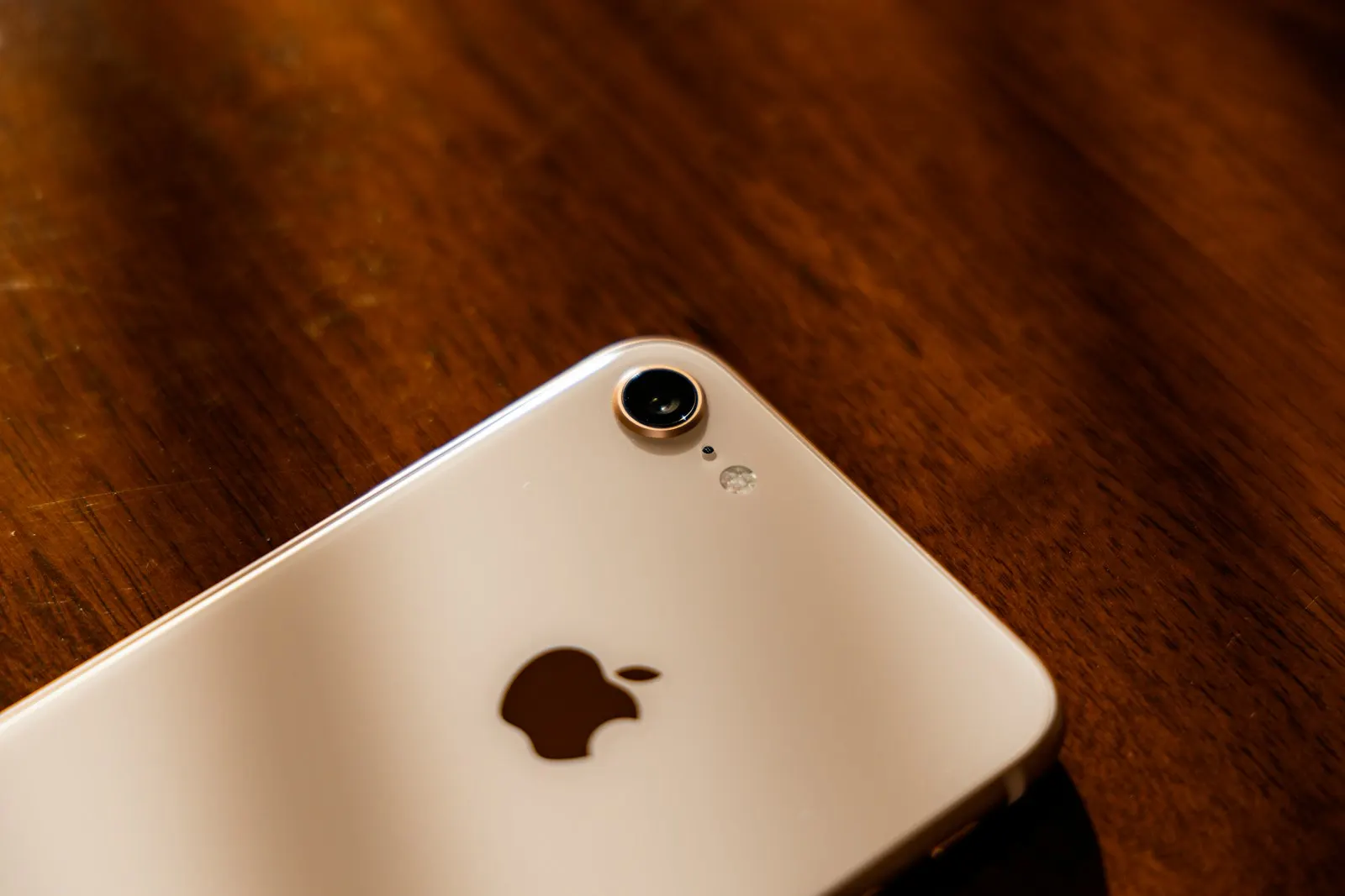 A gold iPhone 8 lying face down on a wooden table