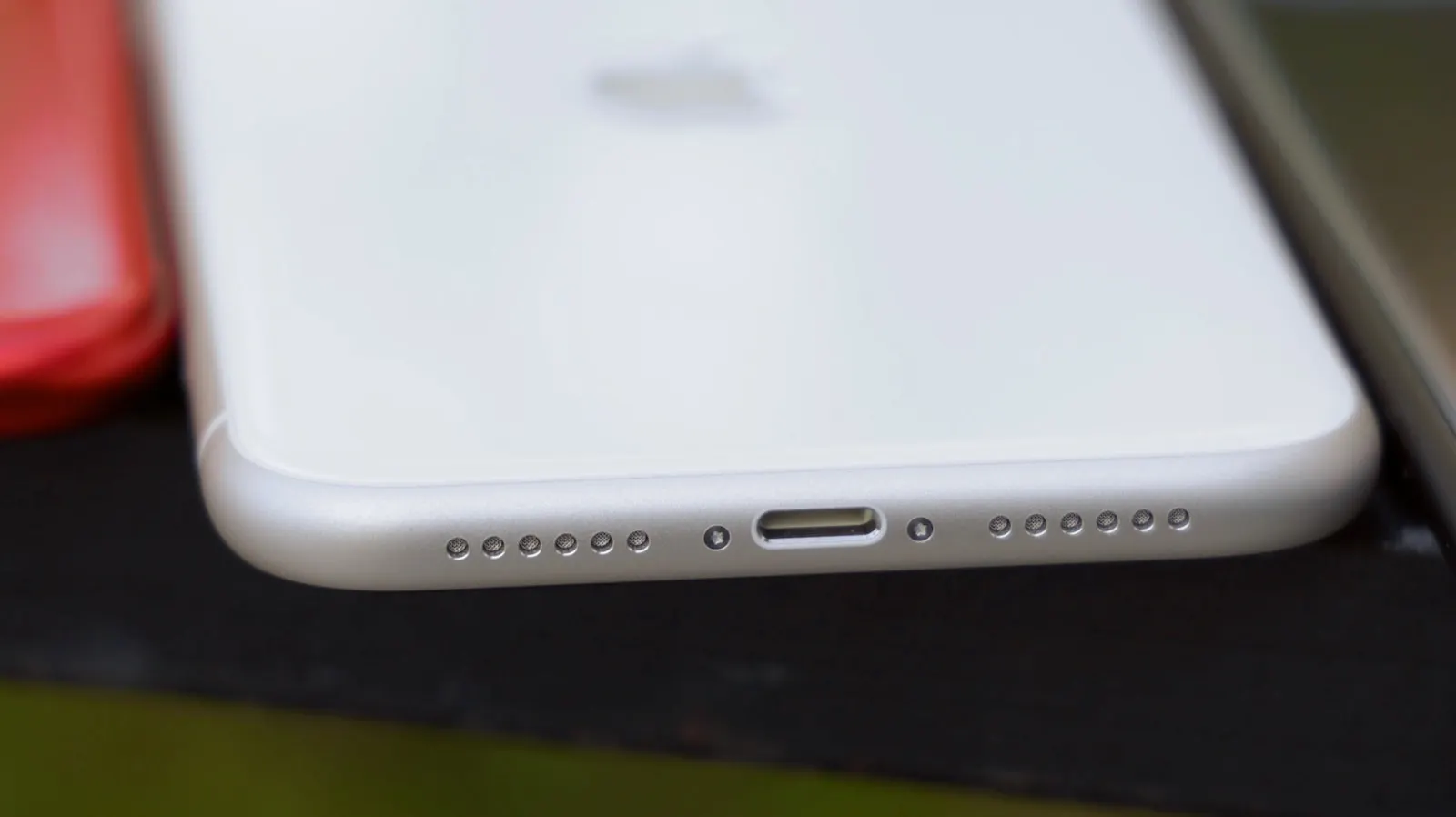 The bottom edge of a white iPhone 11 showing the microphone holes and charging port