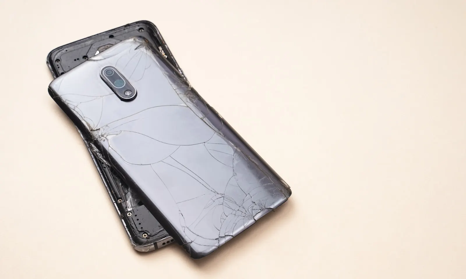 A phone with a shattered back and separated frame on a table