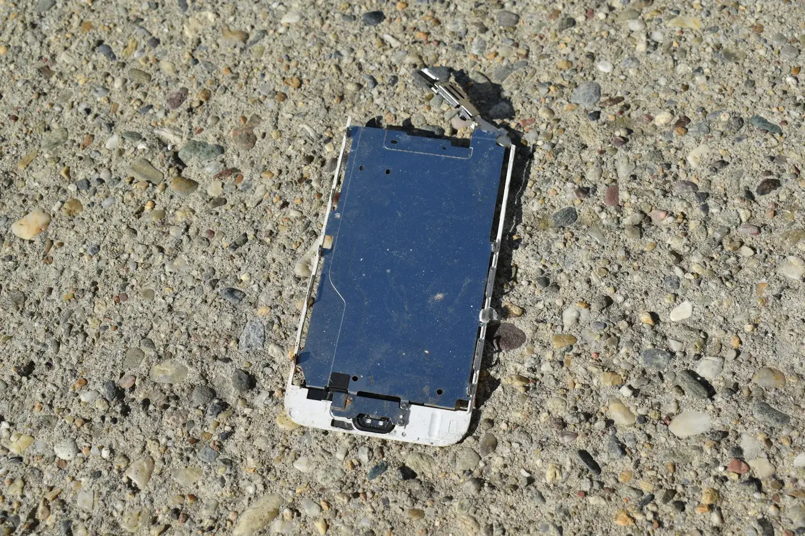 A badly damaged phone with its frame separated, lying on concrete