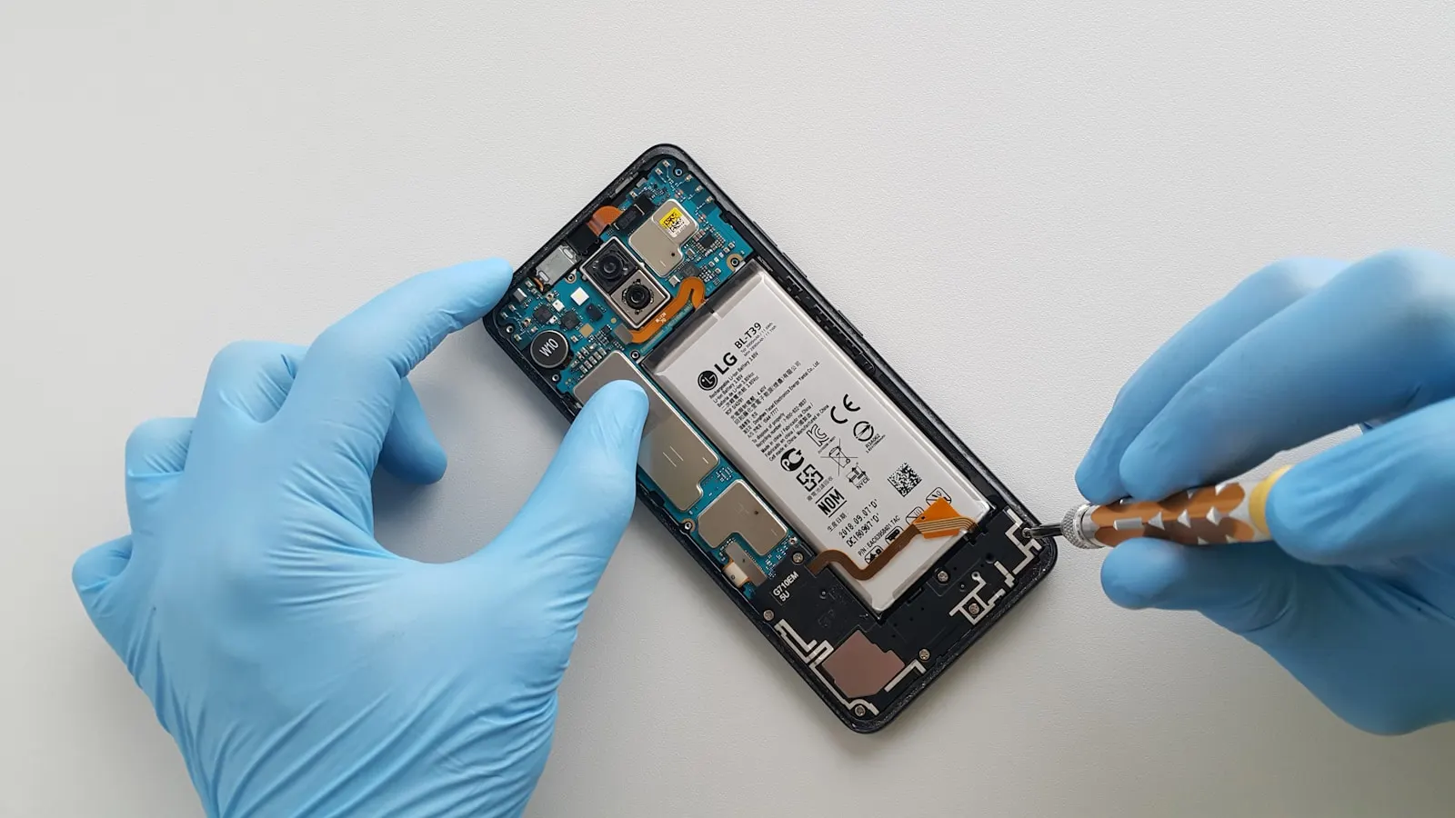 A technician in gloves lifting the battery out of an opened smartphone