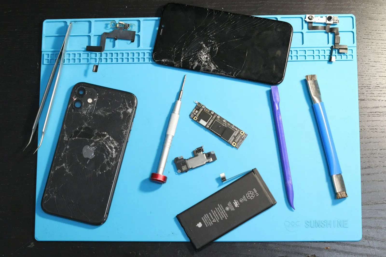 A disassembled iPhone with its battery, screen and tools laid out on a repair mat