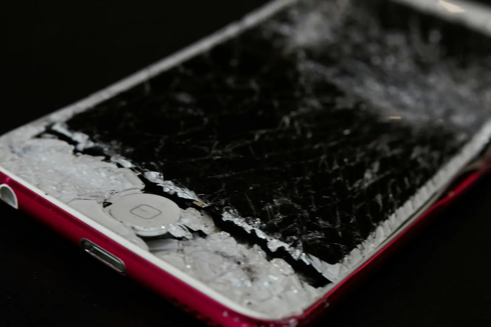 An older iPhone with a shattered screen lying on a dark surface