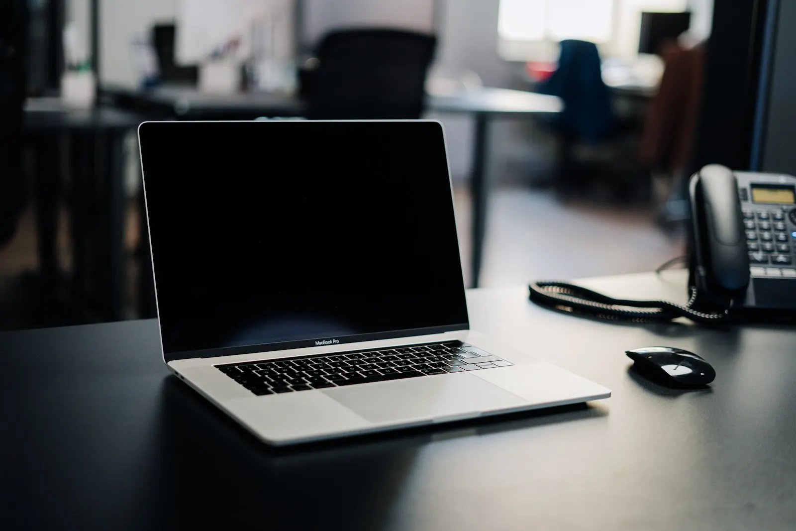 A MacBook Pro with a black screen on an office desk