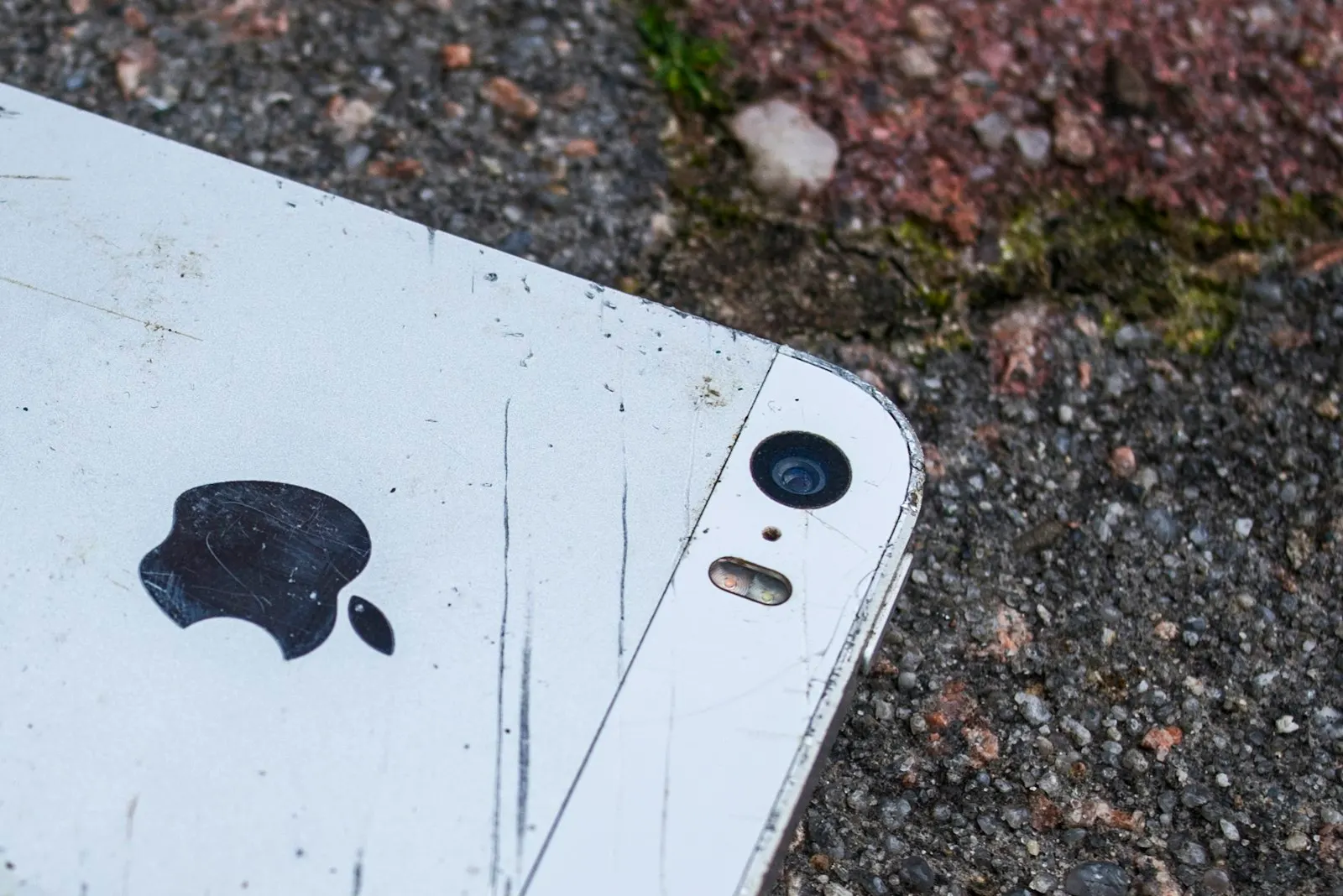 A scratched iPhone lying camera side up on asphalt after a drop