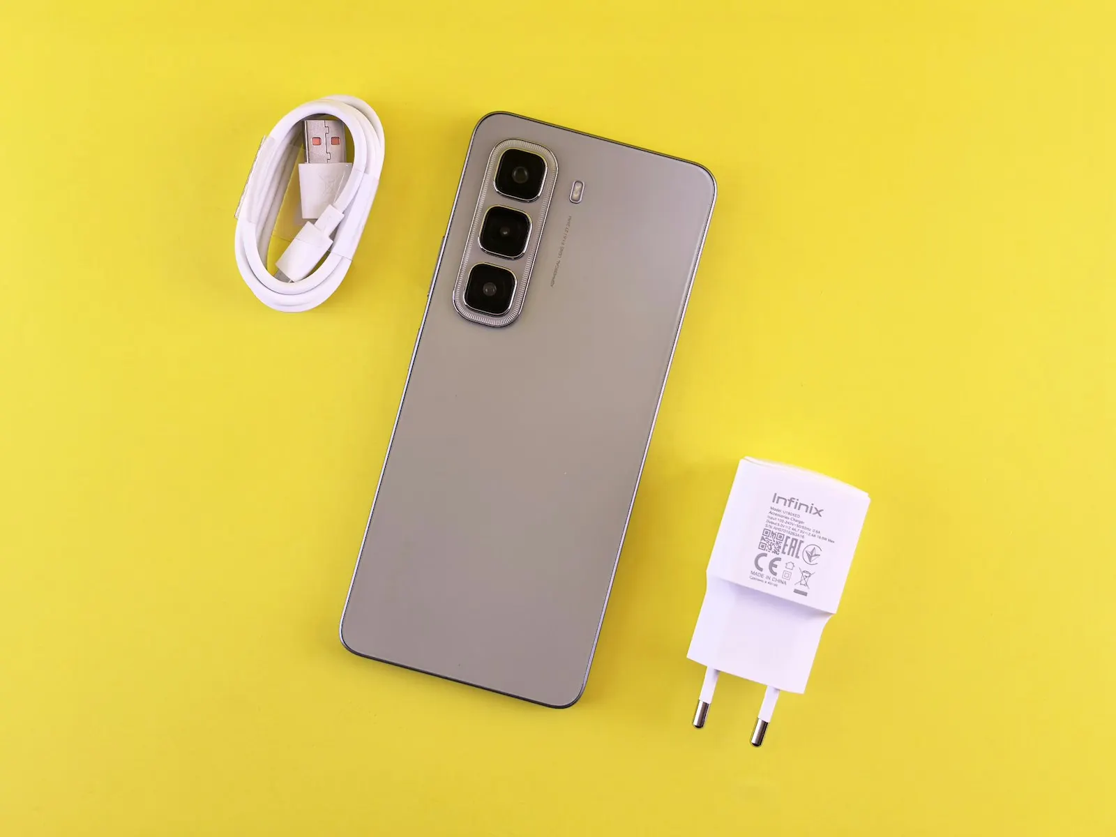 A phone with its charging cable and wall adapter on a yellow background