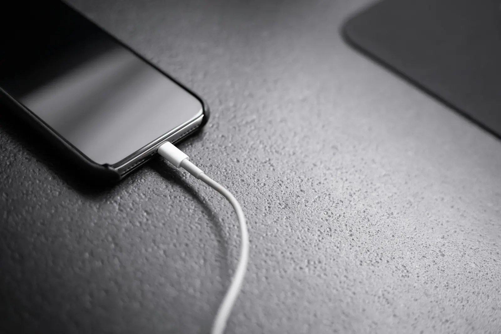 A smartphone with a charging cable connected, lying on a desk