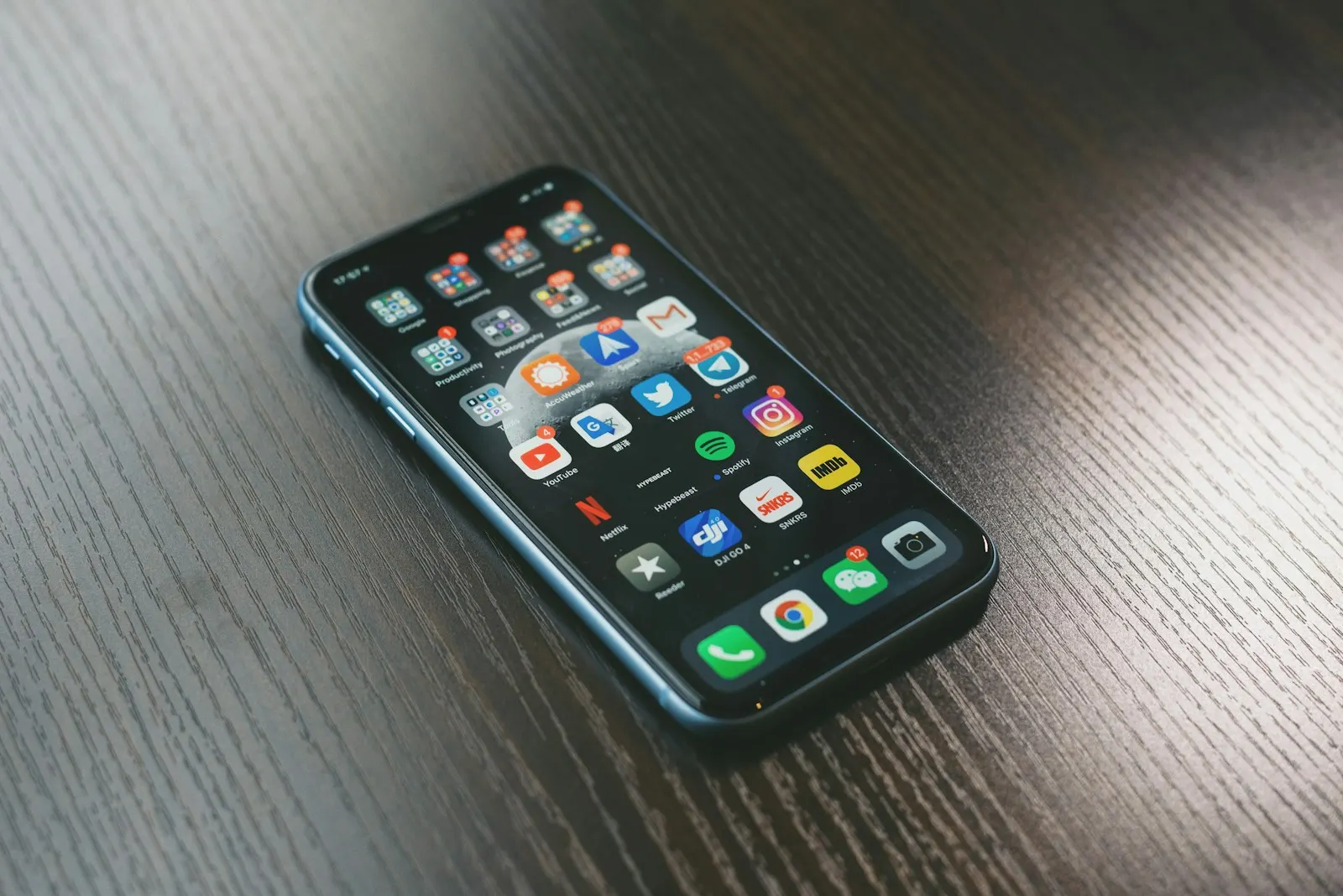 An iPhone lying on a dark wooden table with its home screen on