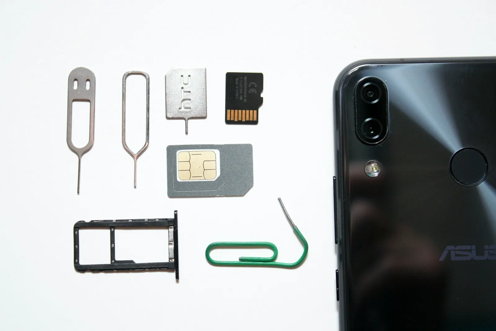 A SIM card, SIM tray and ejector tools beside an Android phone