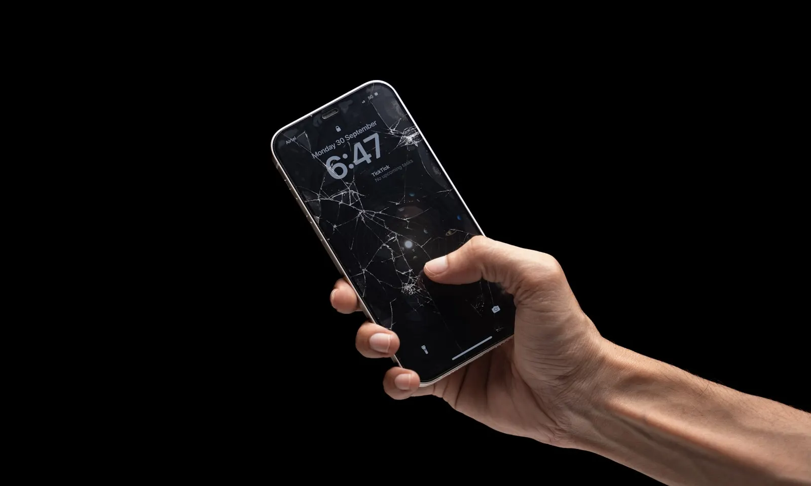 A hand holding a phone with a cracked screen that still lights up