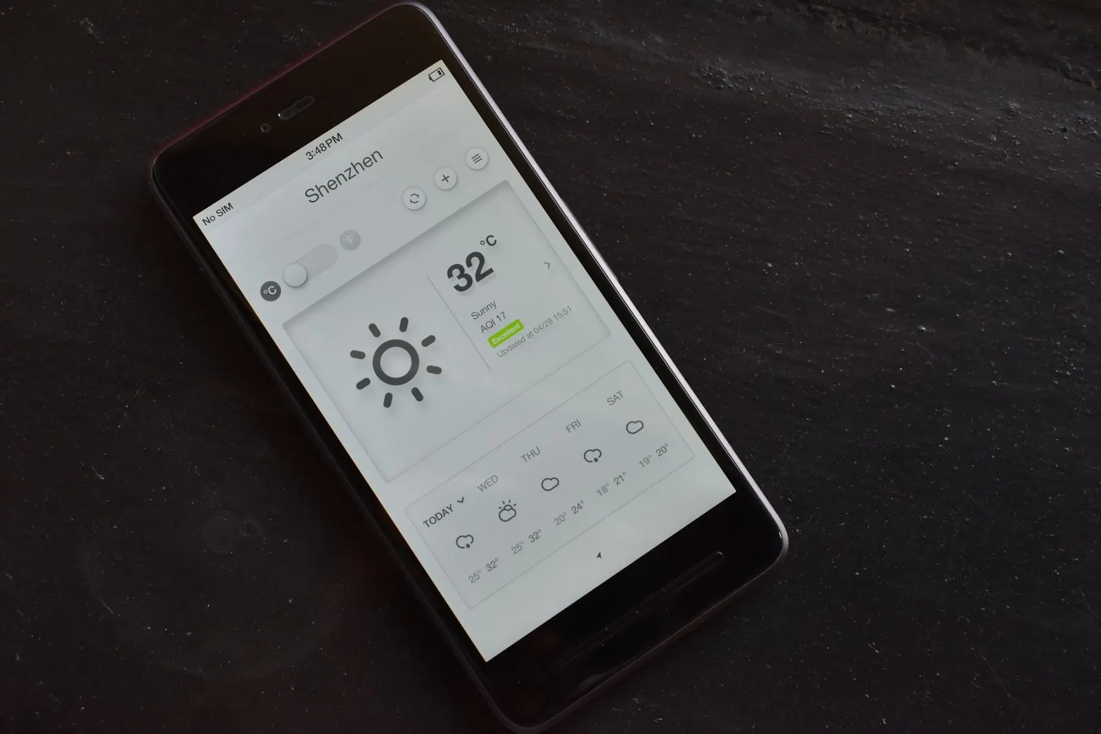 A phone showing a weather app reading 32 degrees on a dark table
