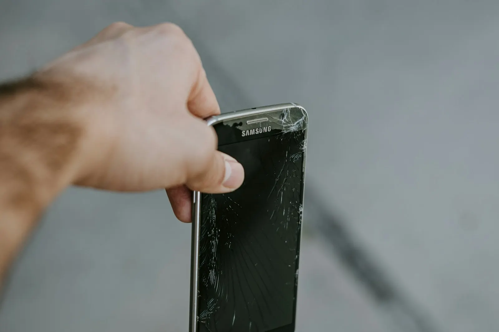 A hand holding a Samsung phone with a badly cracked screen
