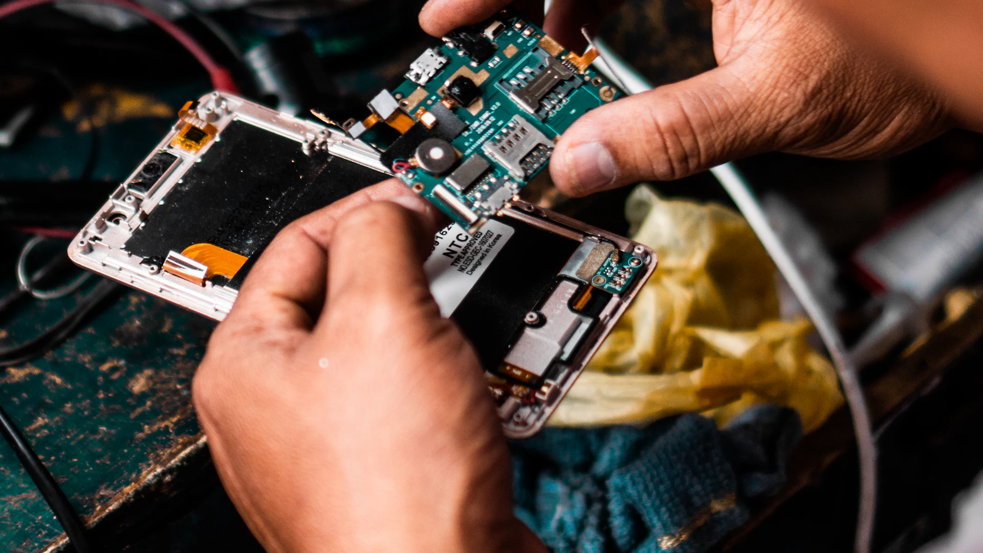 A technician's hands lifting the board out of an opened phone at a repair bench
