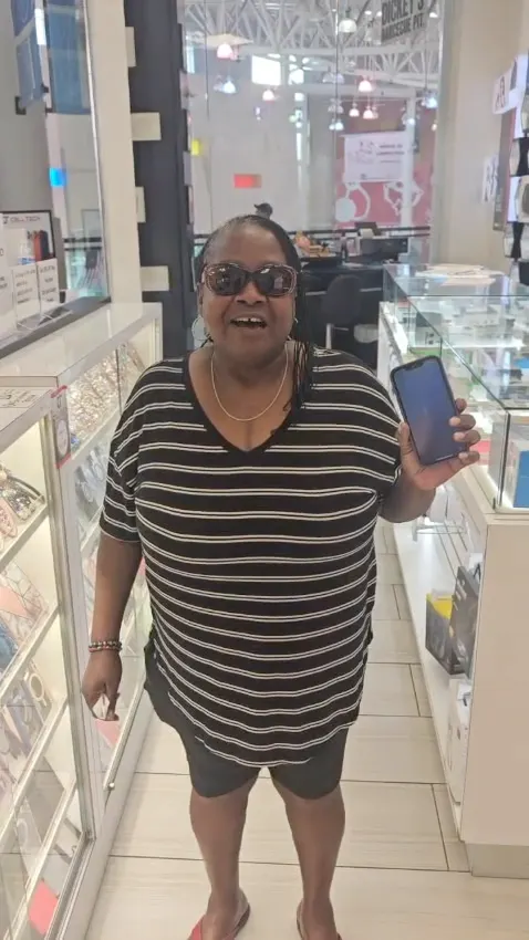 A CELLTECH customer in sunglasses holding up her repaired phone in the Grand Prairie store