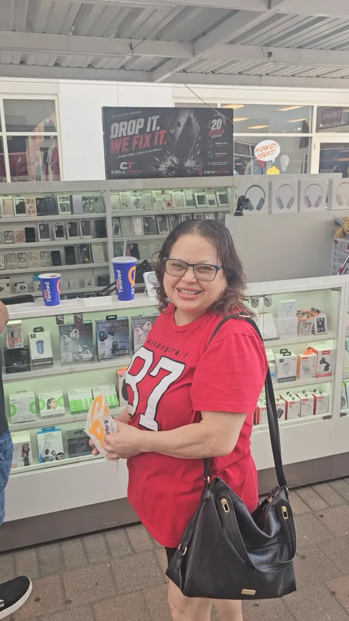 A CELLTECH customer in glasses smiling in front of the Grand Prairie outlet kiosk