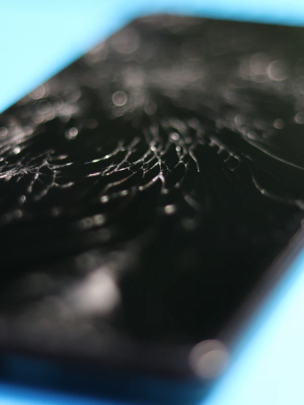 A shattered phone screen lit from the side, cracks spreading across the glass