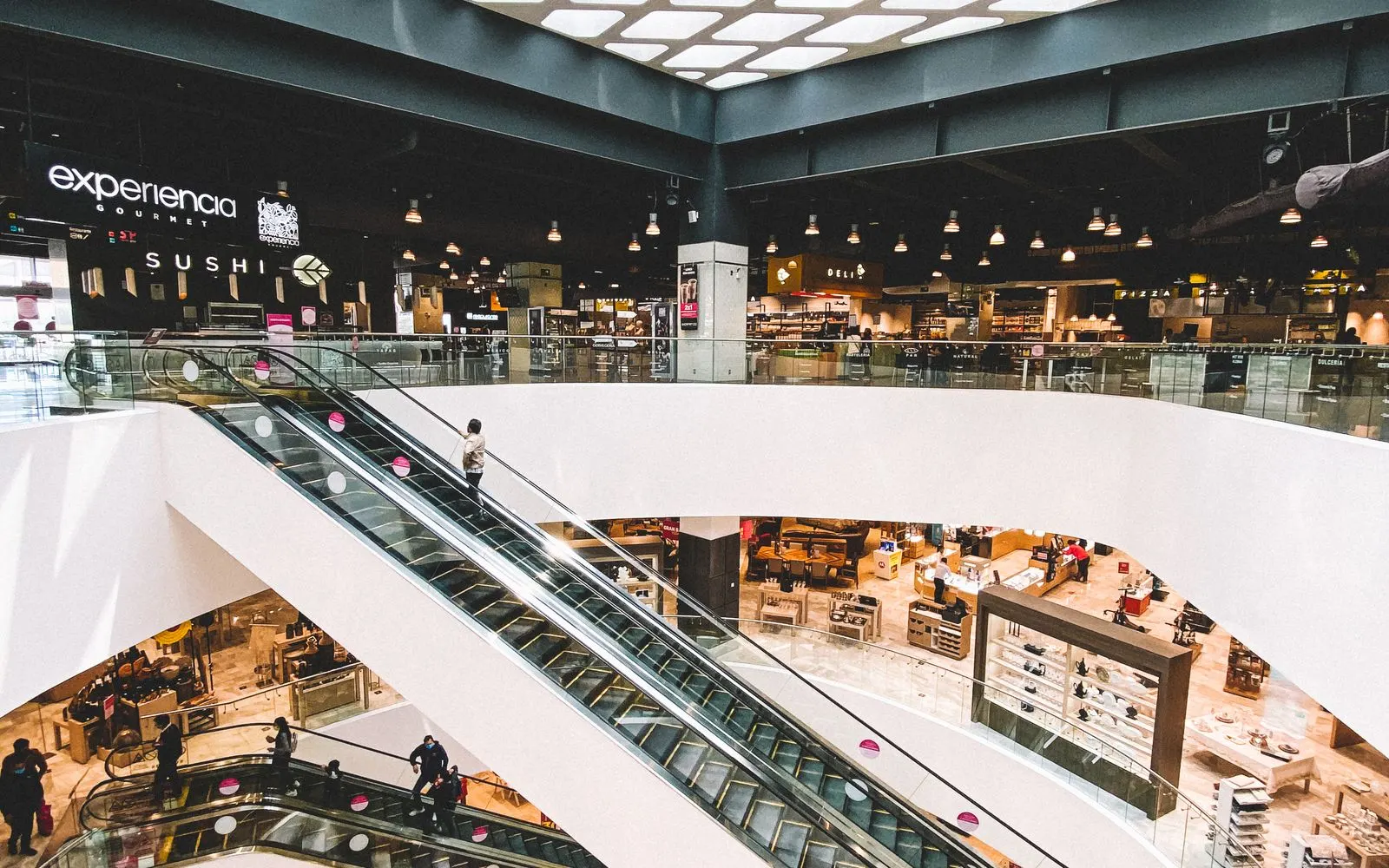 Escalators linking the floors of a bright indoor shopping mall lined with stores and places to eat