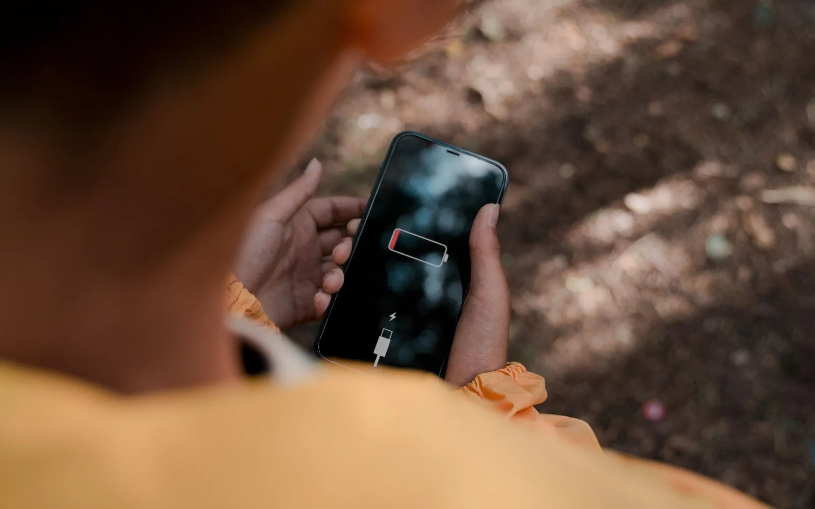Looking over a shoulder at an iPhone showing the empty battery and connect to power screen