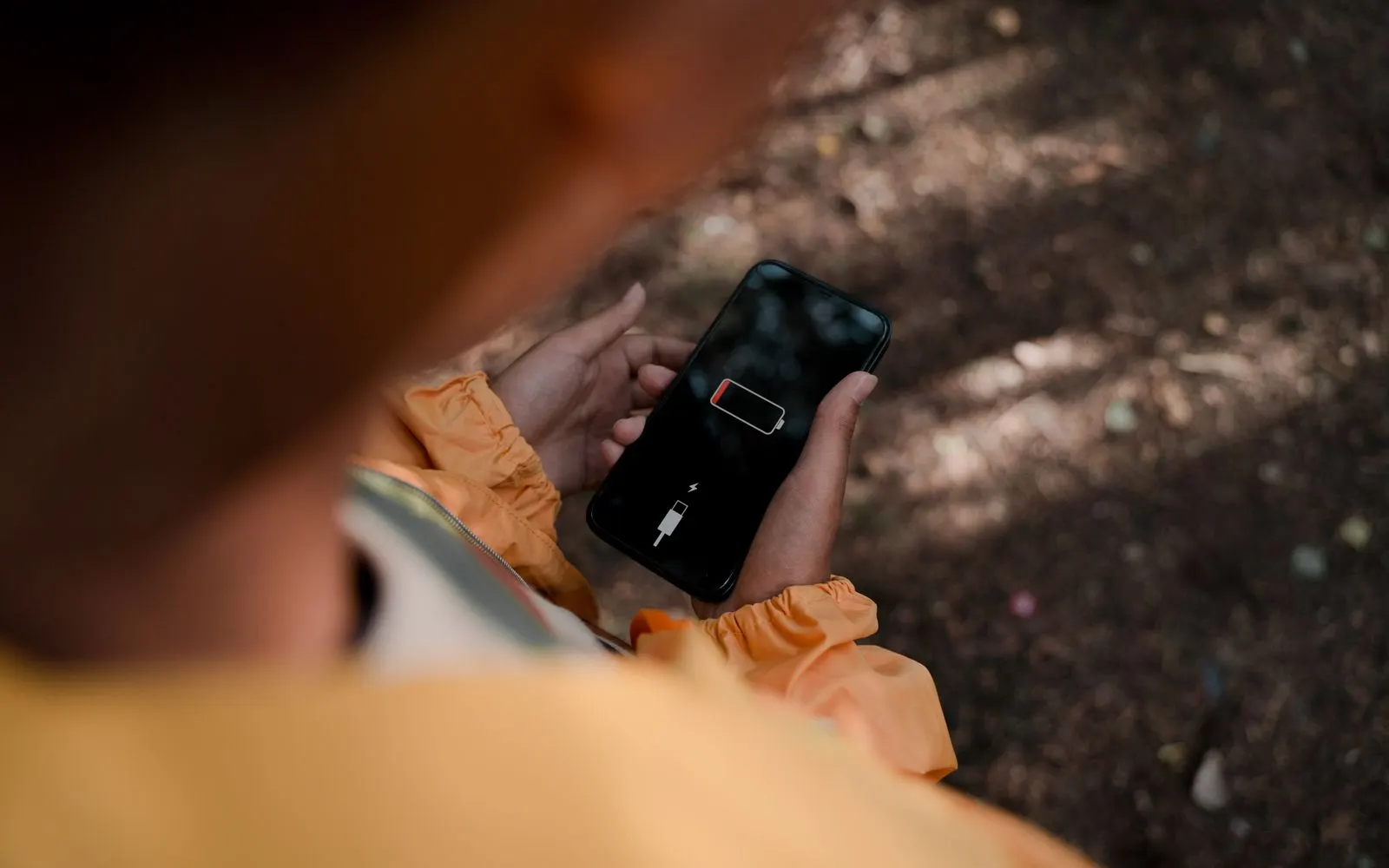An iPhone held in both hands showing the empty battery and connect to power screen