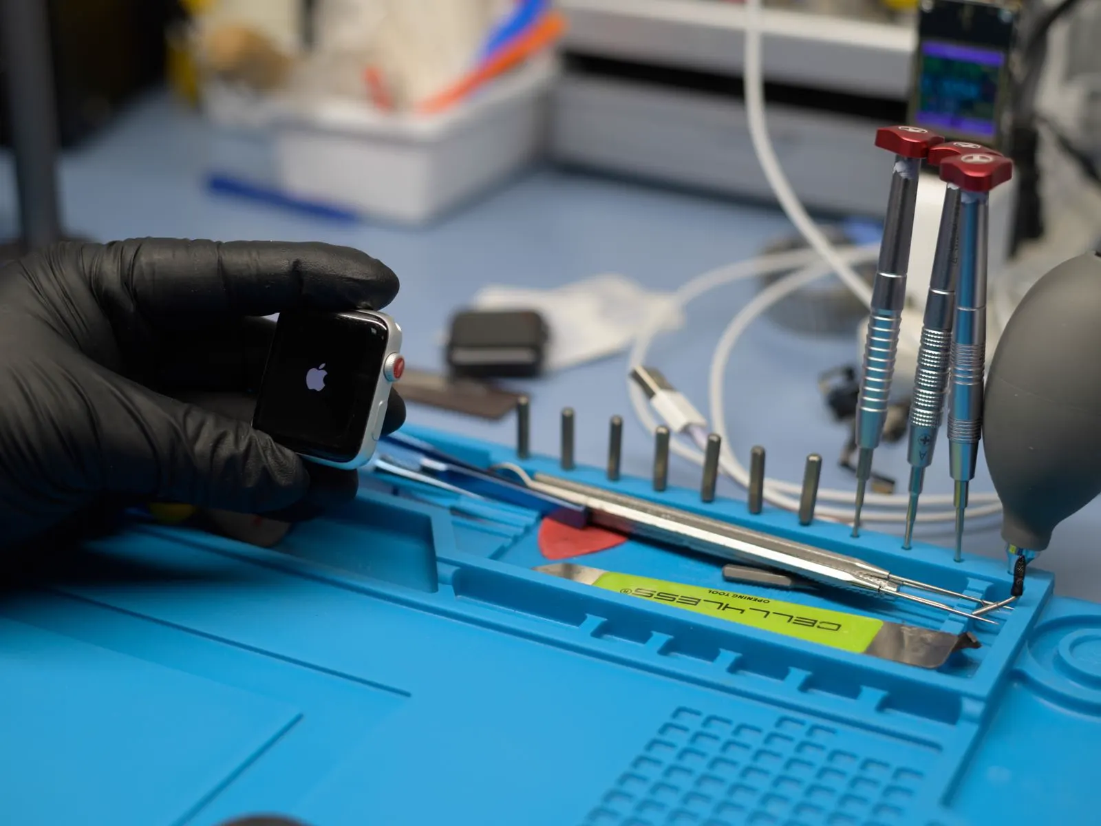 A technician in black gloves working on a phone at a repair bench, tools laid out beside it