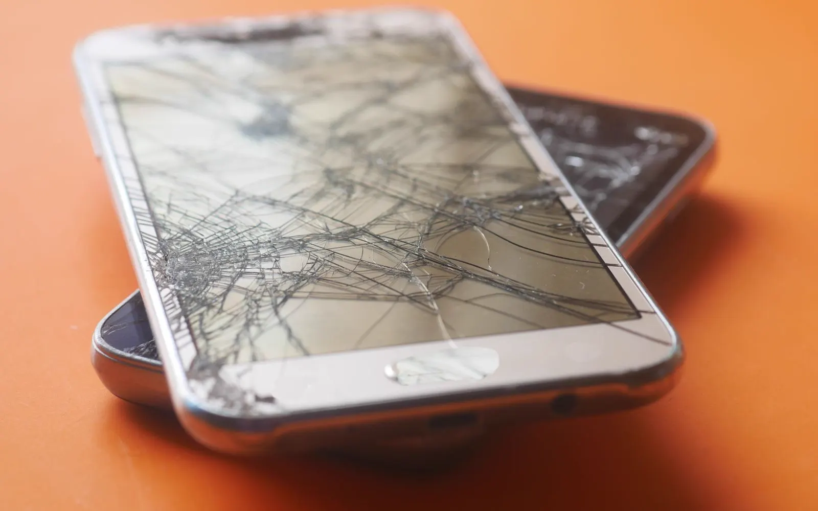Two damaged smartphones on an orange background