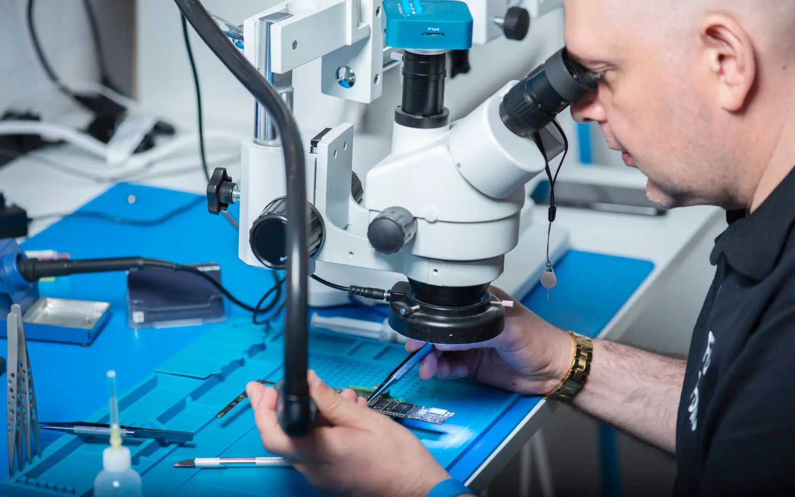 A technician looking through a microscope while working on a phone at a blue repair bench
