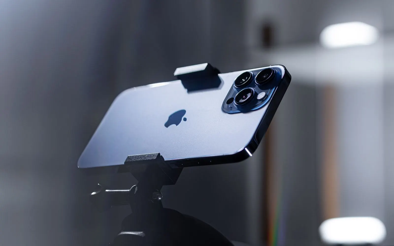 A blue iPhone Pro held in a tripod clamp, its triple rear camera facing the room