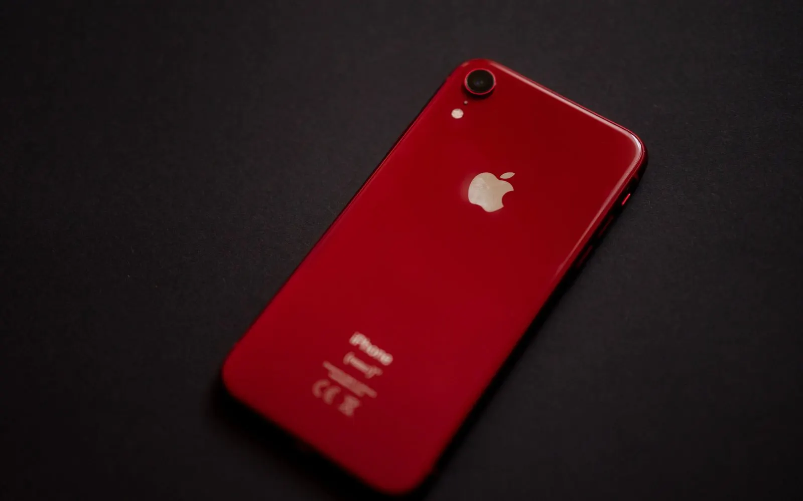 The red glass back of an iPhone XR lying on a black surface
