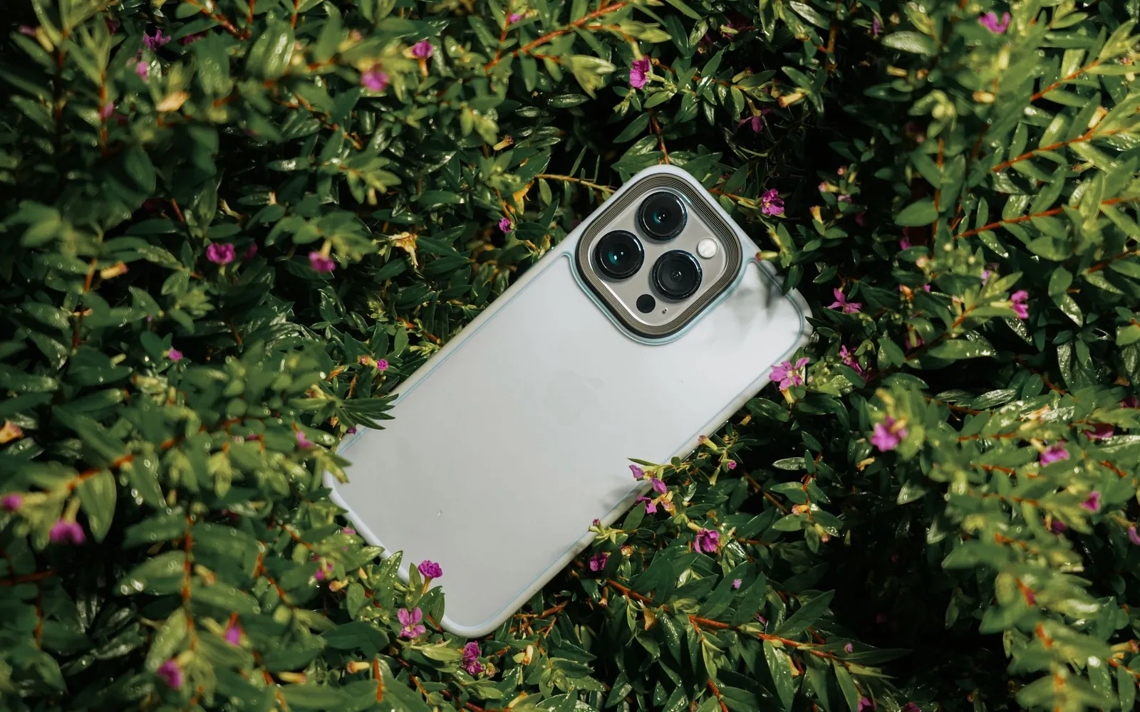 A white iPhone Pro in a clear case resting in a green shrub