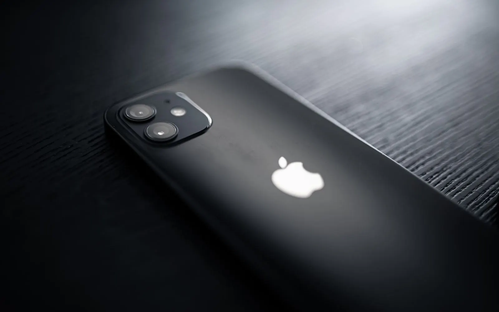 The back of a black dual camera iPhone lying on a dark wooden table