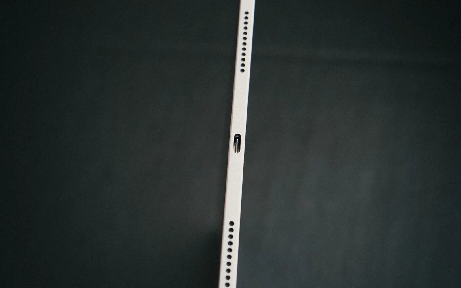 A hand holding a slim tablet against a dark backdrop
