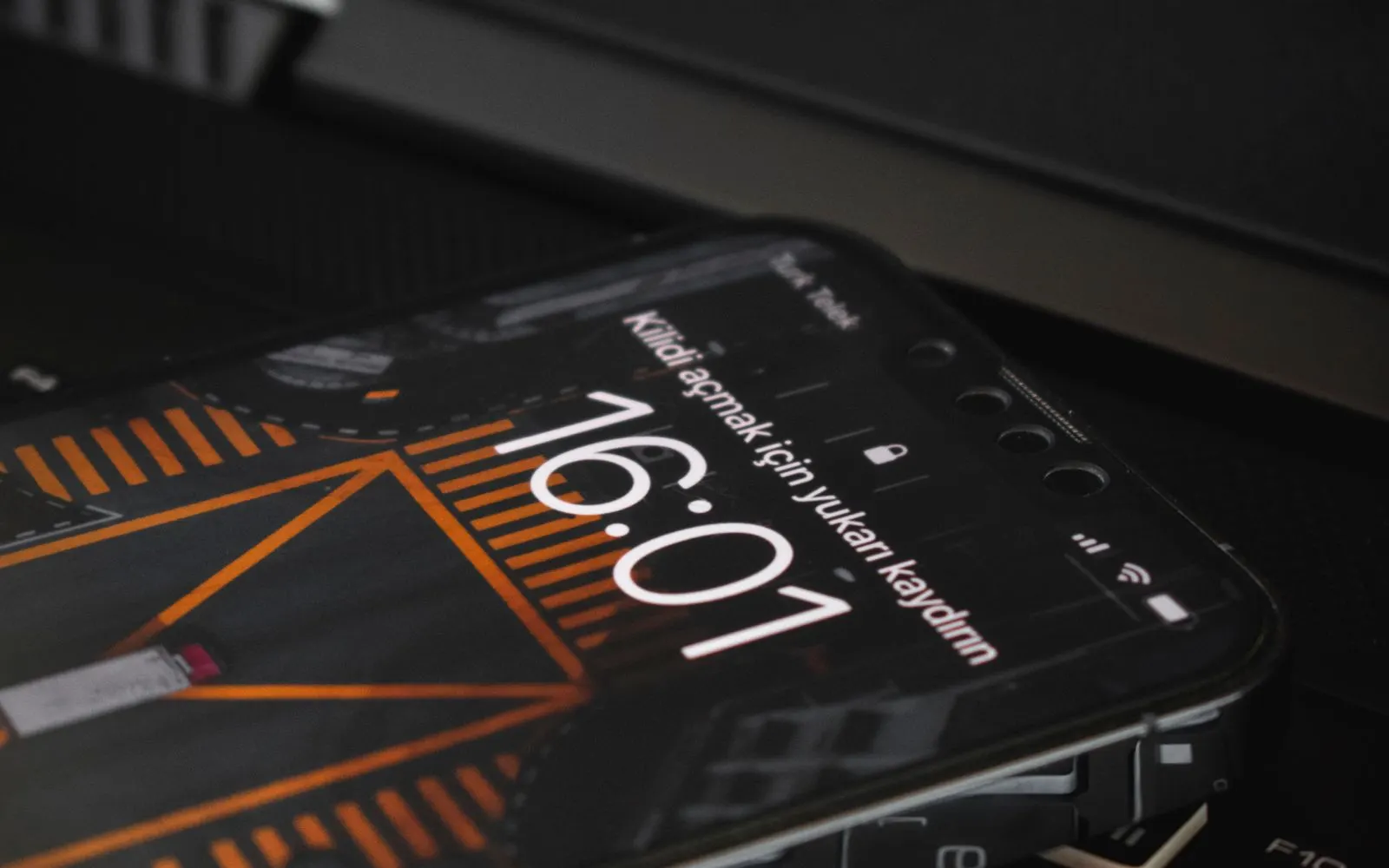 A smartphone lock screen showing the time 16:01 on a dark surface