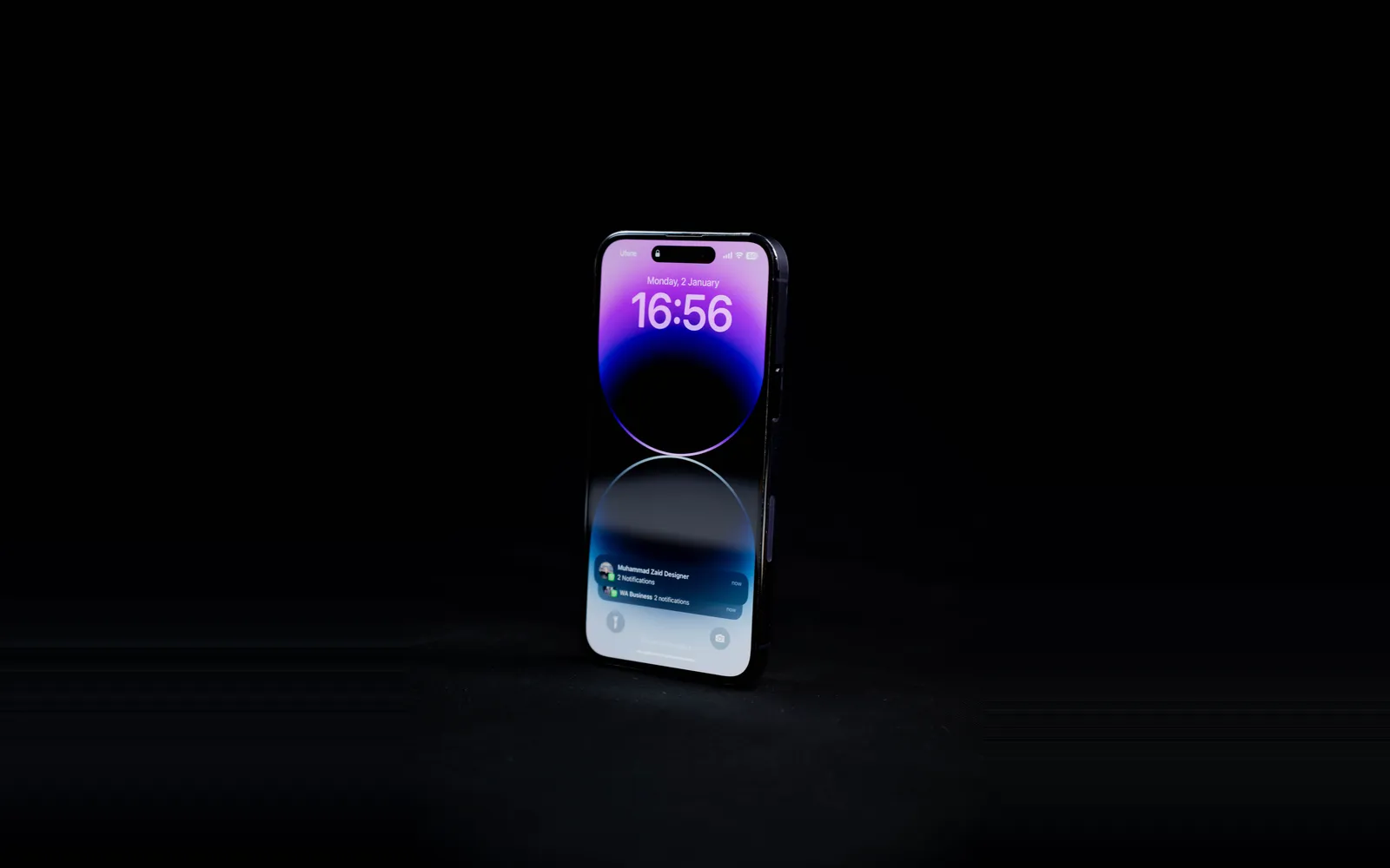 An iPhone Pro standing upright on a black surface, its lock screen lit with the Dynamic Island at the top