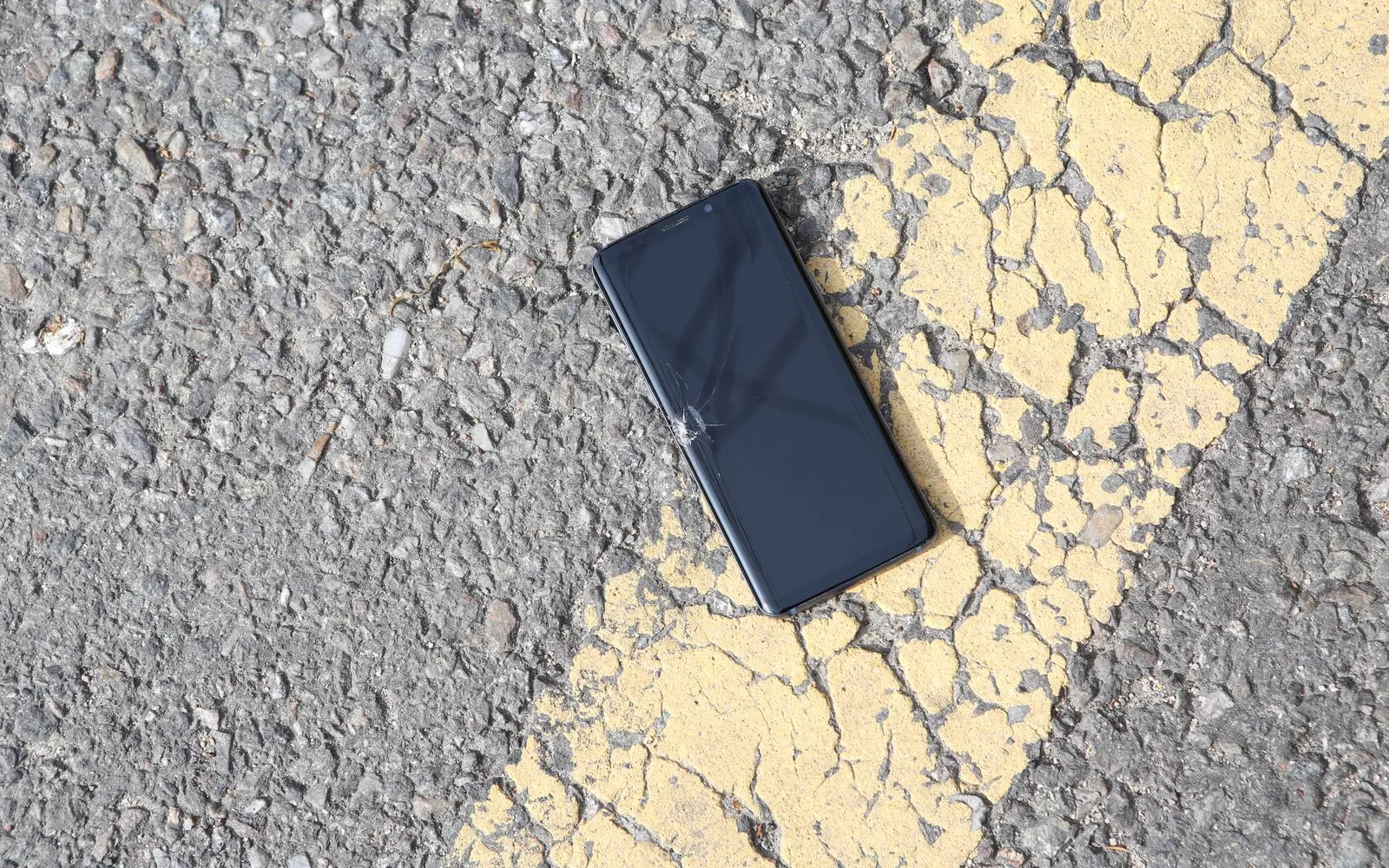 Un smartphone con la pantalla rota sobre el asfalto bajo el sol