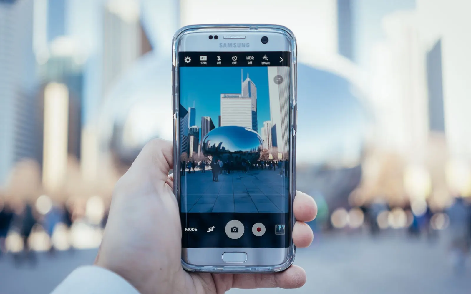 A hand holding up a Samsung Galaxy with a curved edge screen, its camera app open on a city street