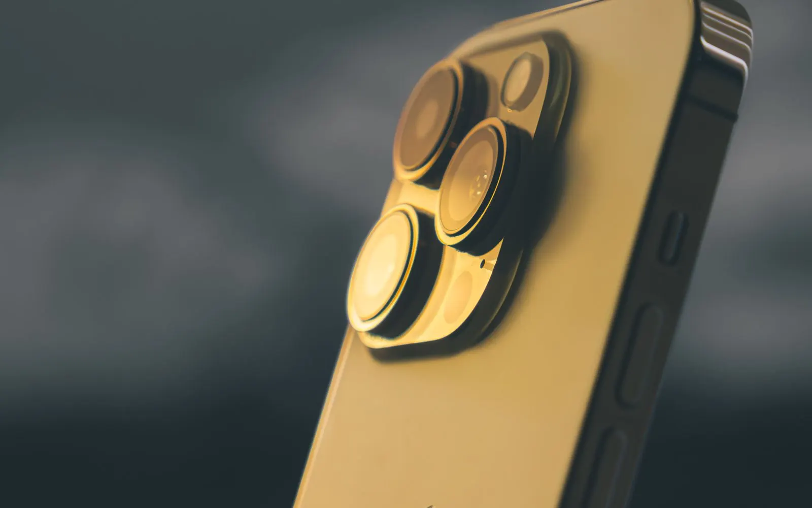 The rear cameras of a gold iPhone Pro against a dark grey backdrop
