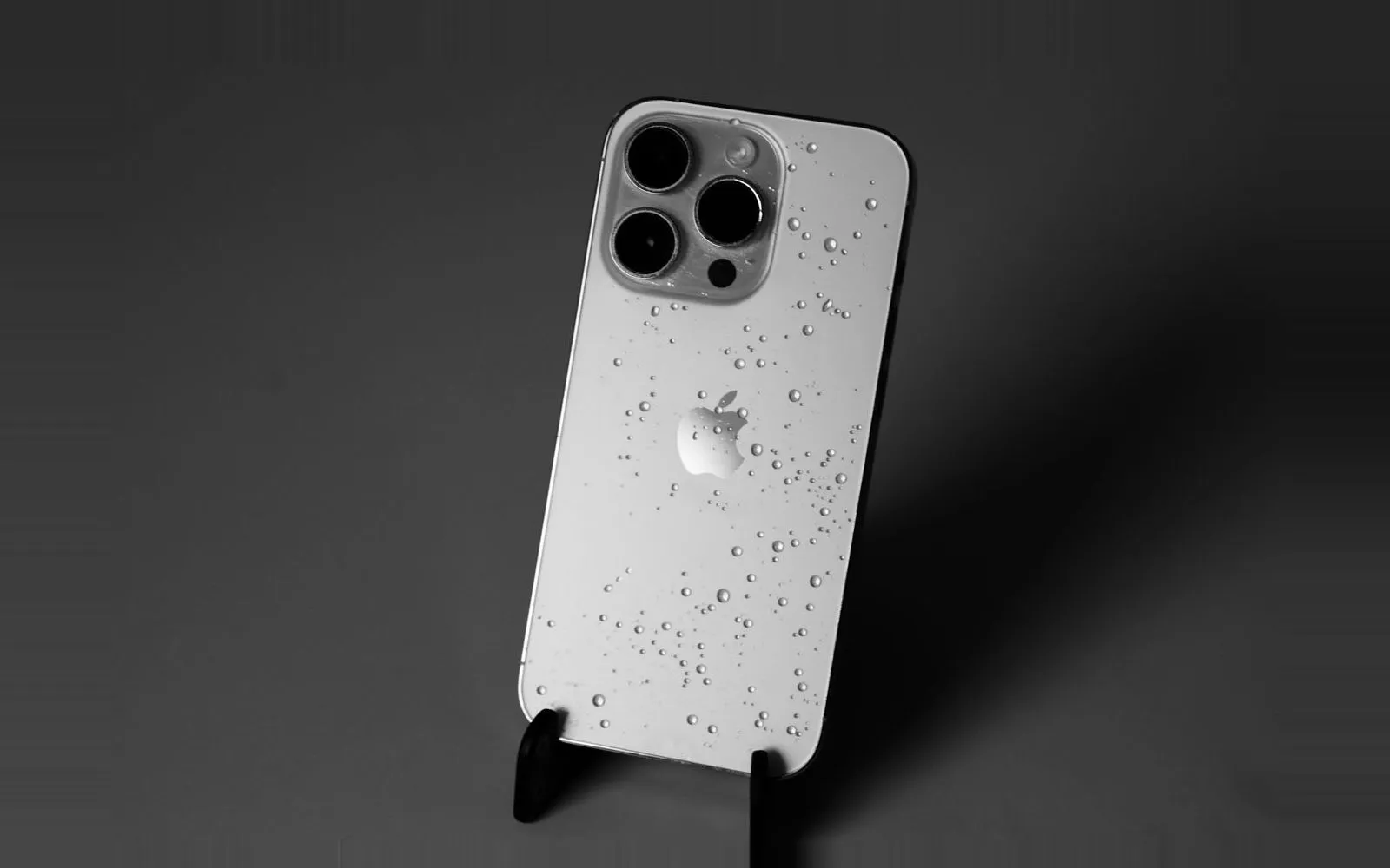 A white iPhone Pro on a stand, its back glass covered in water droplets