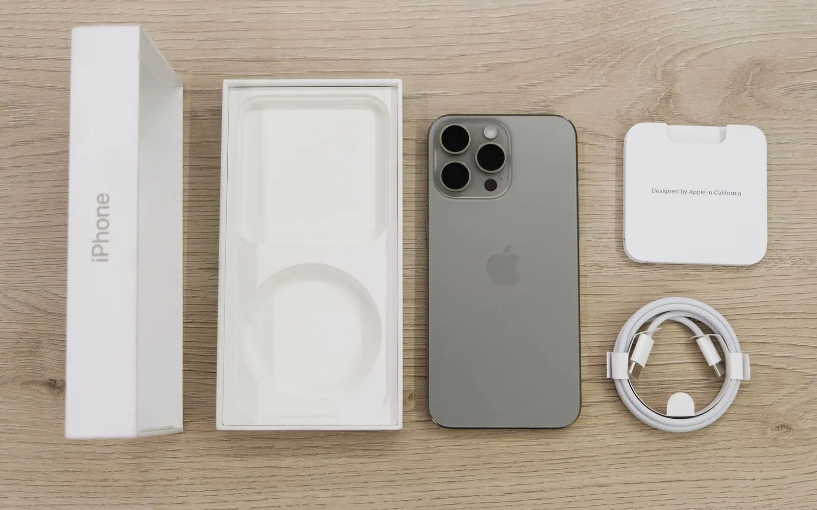 A titanium iPhone Pro laid out beside its opened box and USB-C cable on a wooden table