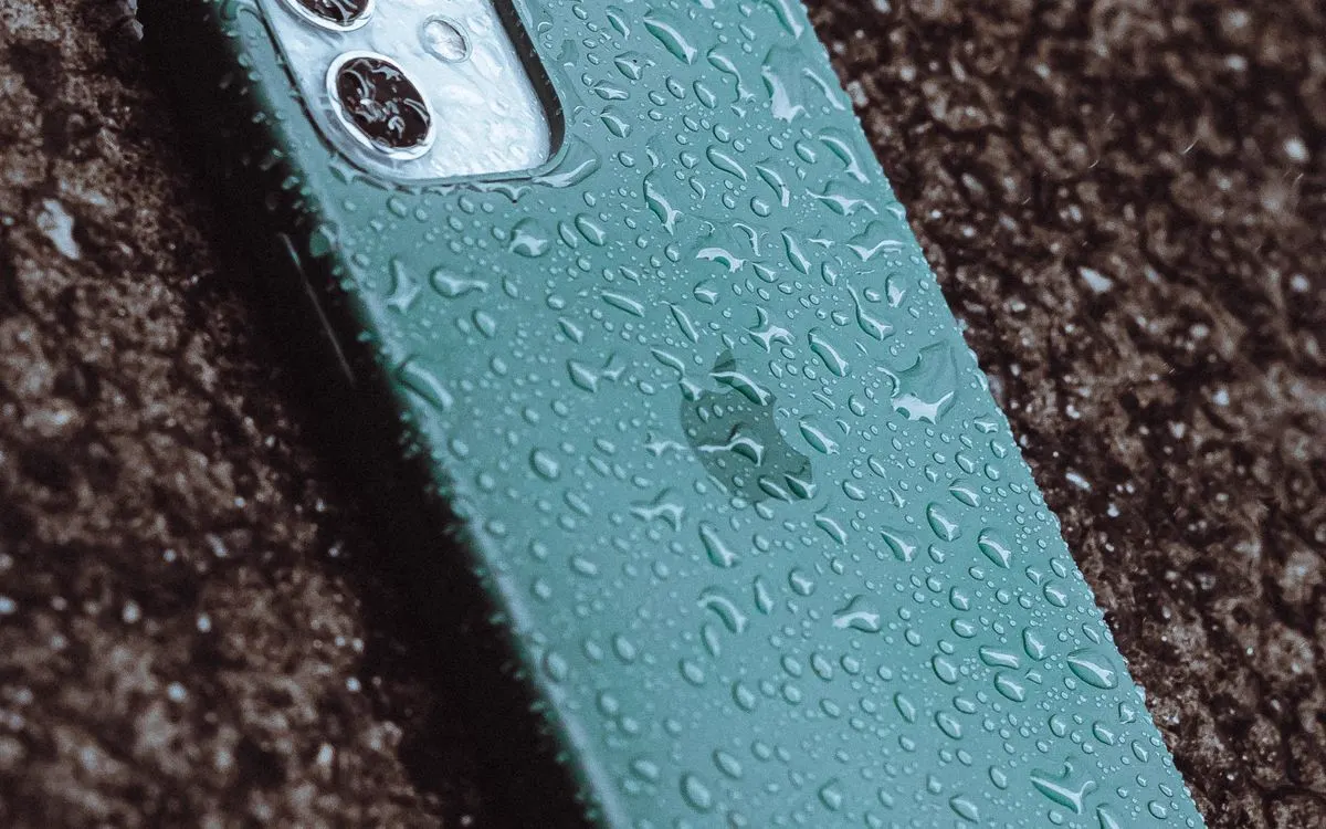 Raindrops beaded across the screen of a wet smartphone