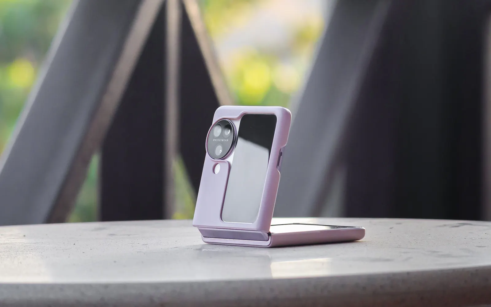 A lavender Samsung Galaxy Z Flip standing half open on a round outdoor table