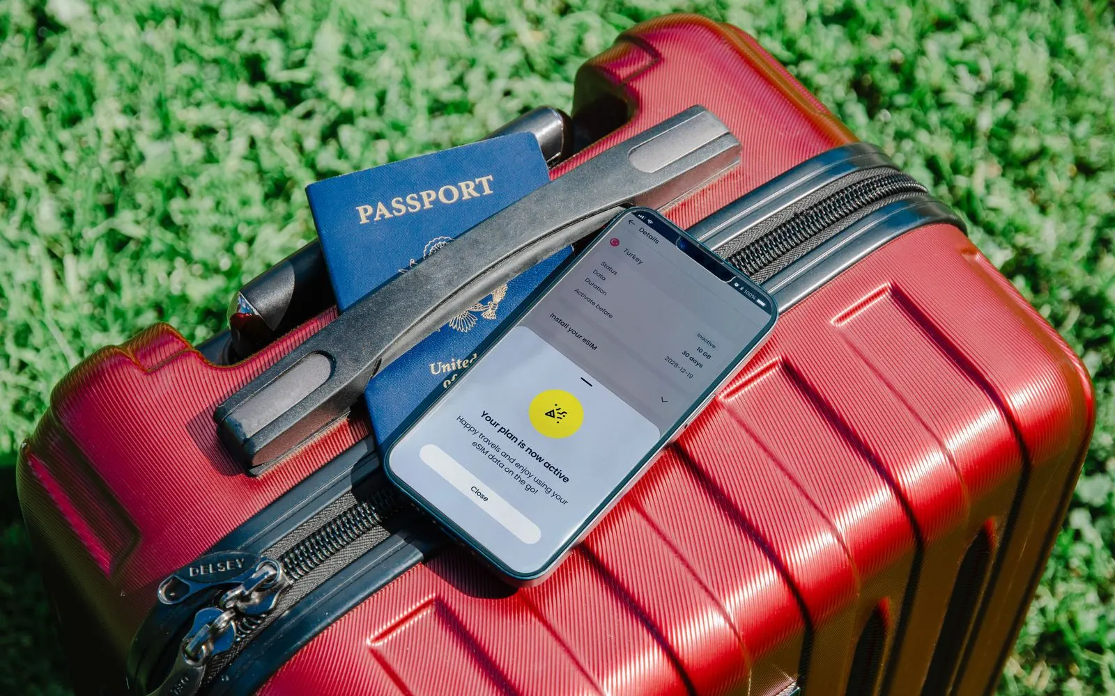 A passport and an iPhone resting on a red suitcase on the grass