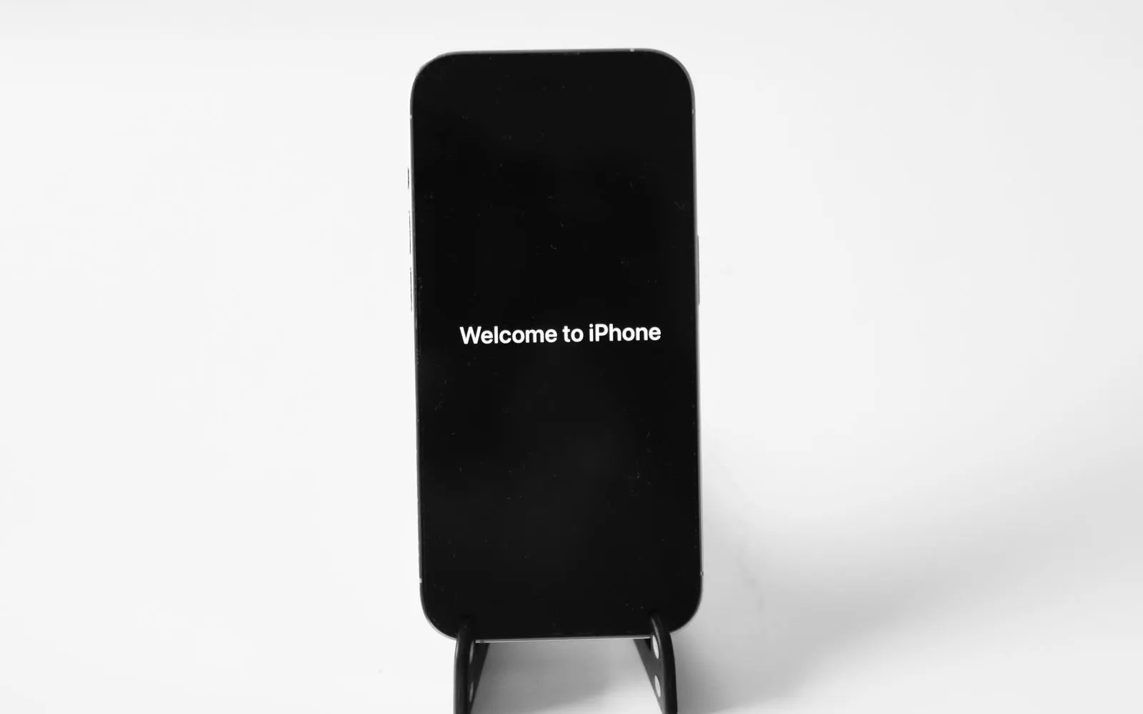 An iPhone on a small stand showing its Welcome to iPhone screen against a white background