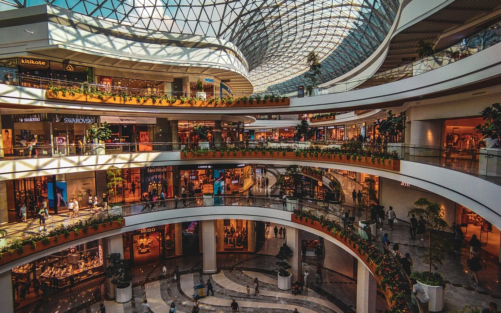 The upper levels of an indoor shopping mall ringed with stores under a glass roof