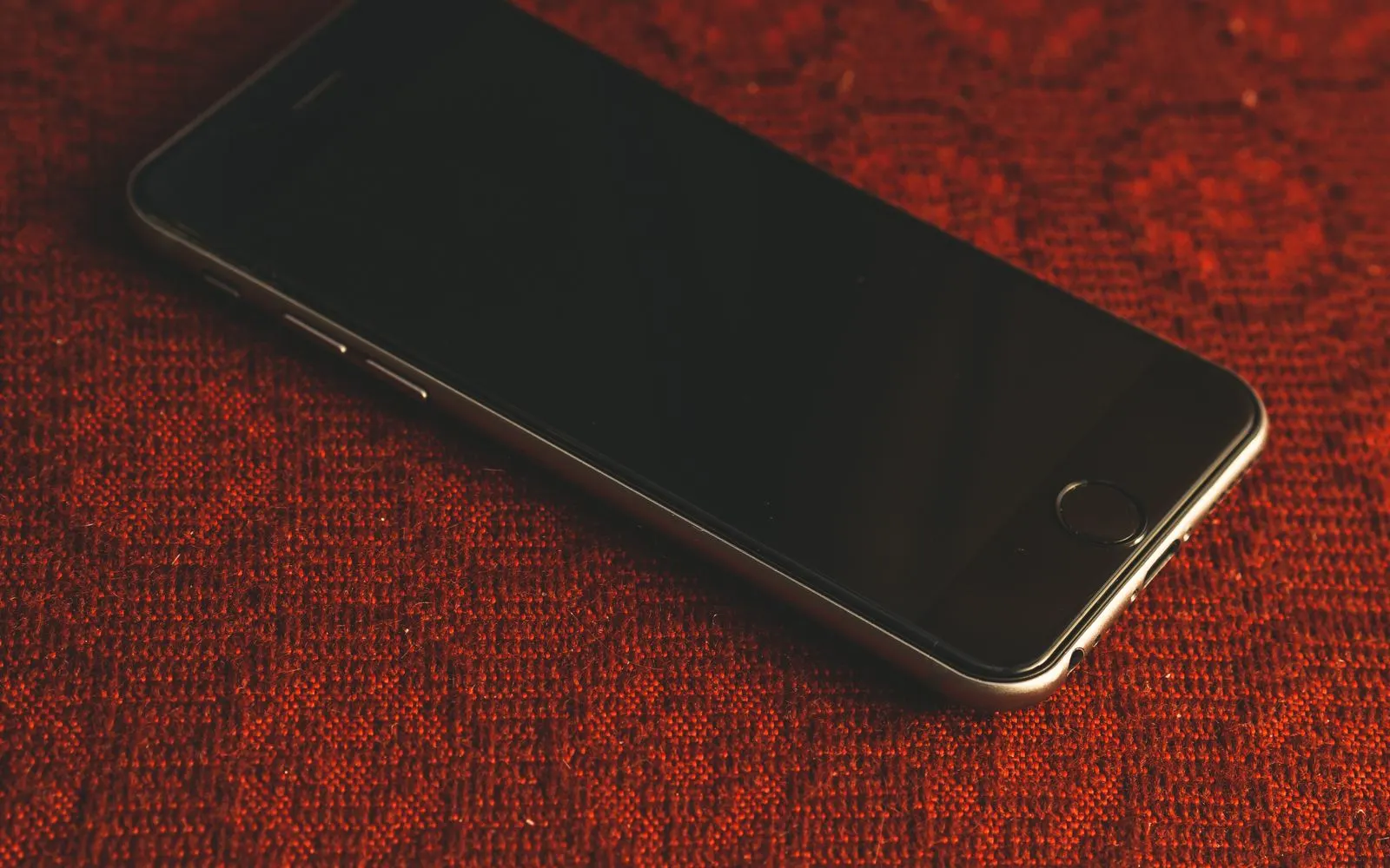An iPhone lying on a red fabric surface with its screen completely black