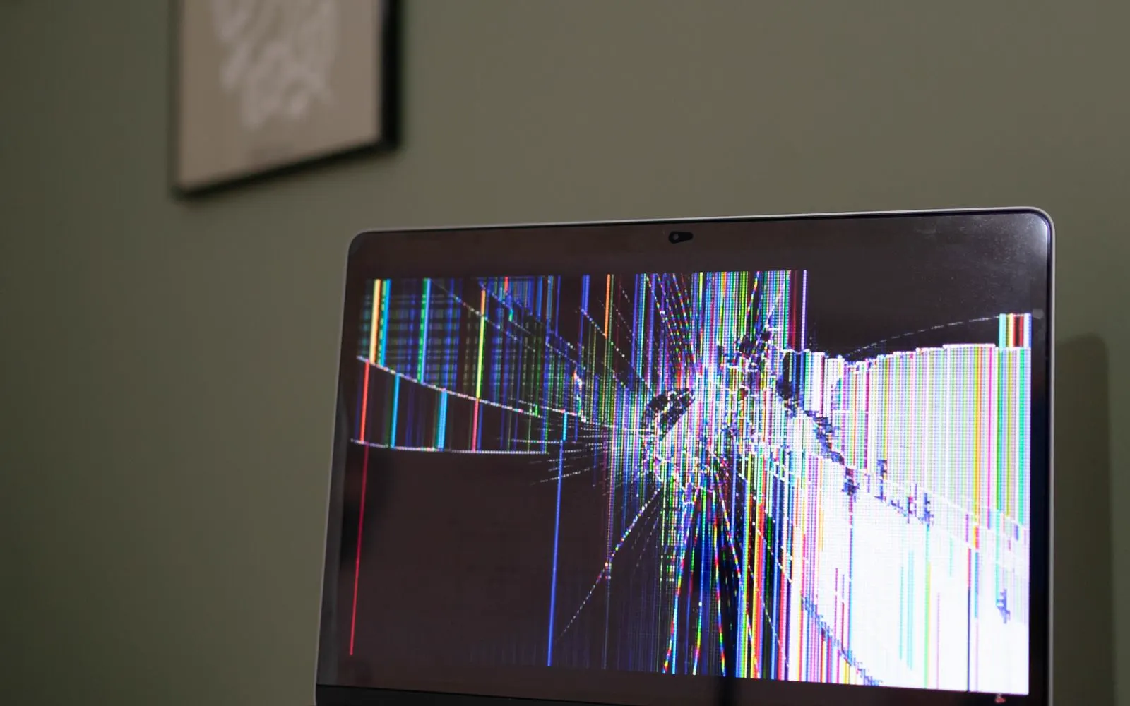 A laptop on a desk with a cracked, malfunctioning screen