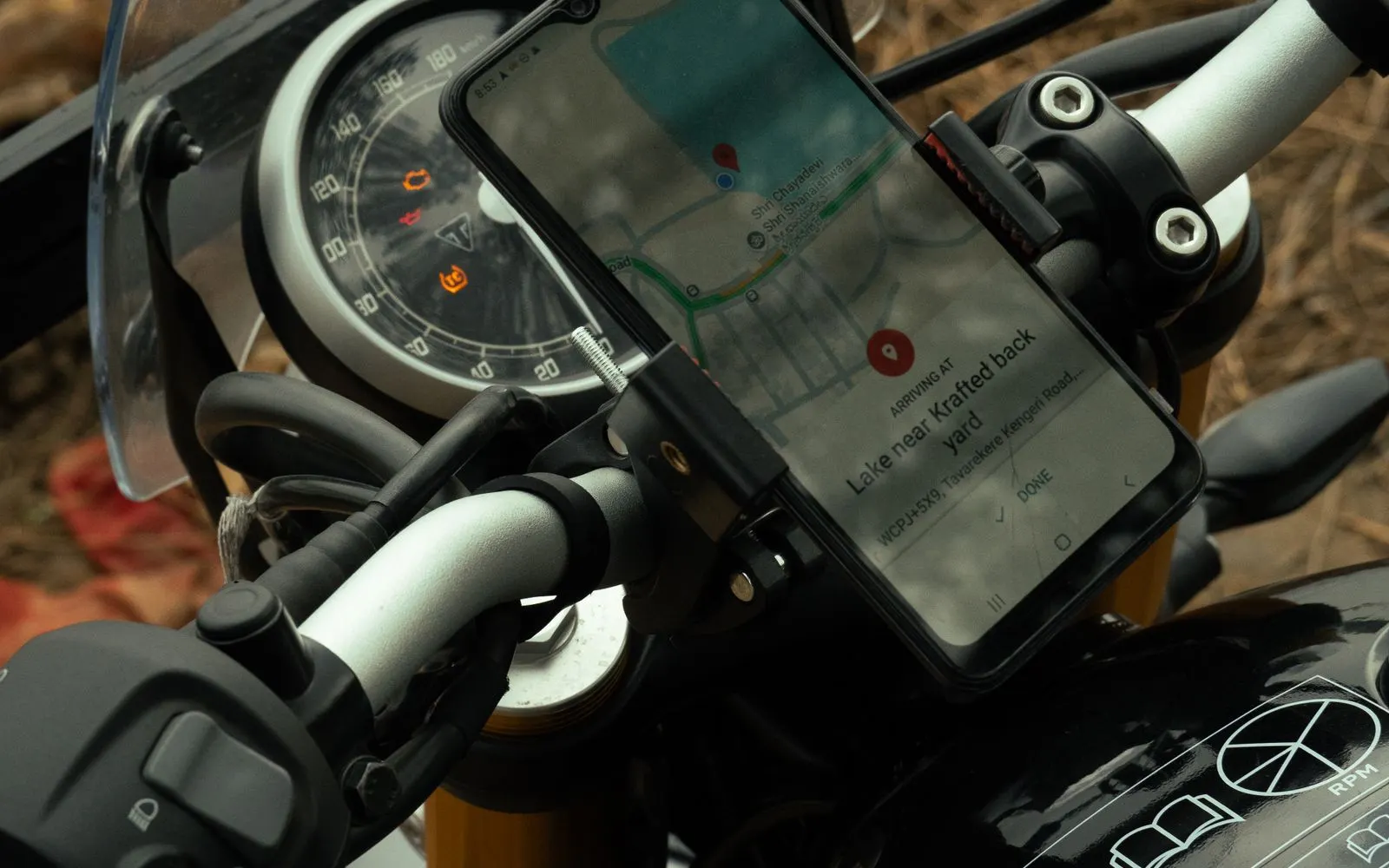 A phone showing a map, clamped in a mount on a motorcycle handlebar beside the speedometer