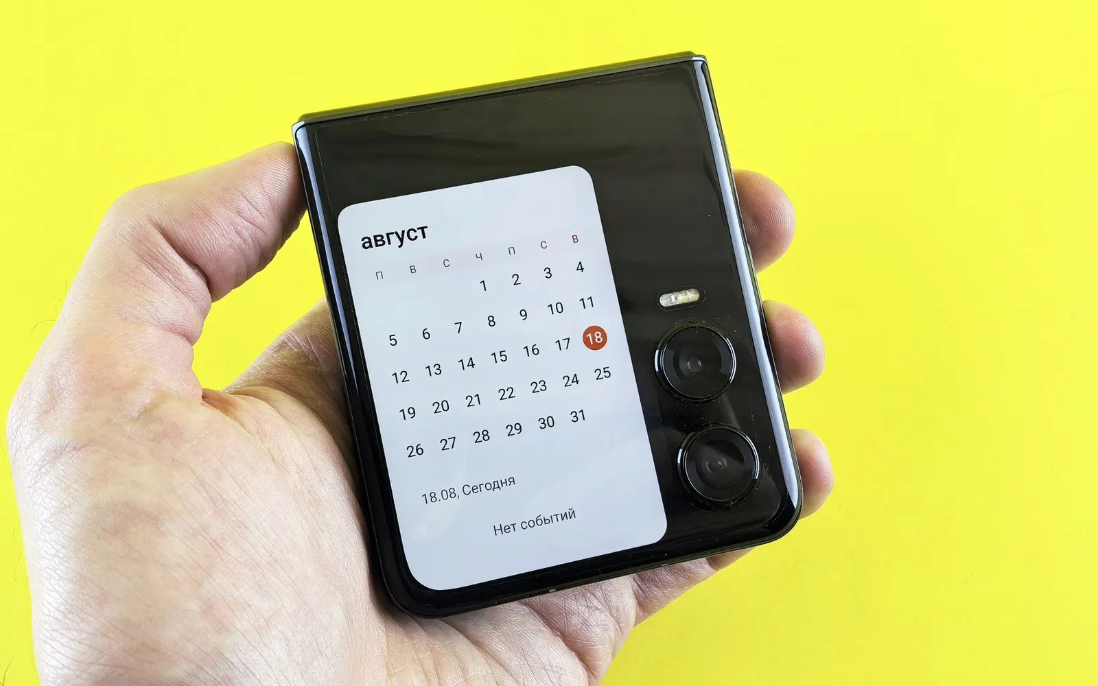 A Samsung Galaxy Z Flip folded shut in a hand, a calendar showing on its cover screen