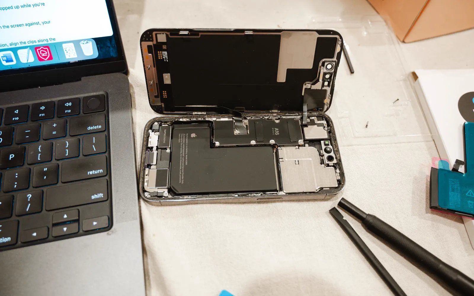 An opened iPhone on a bench beside repair tools and a laptop